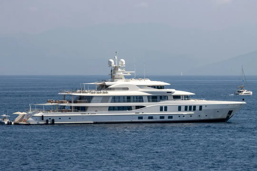 White motor yacht at anchor in calm blue water with hazy coastal mountains behind
