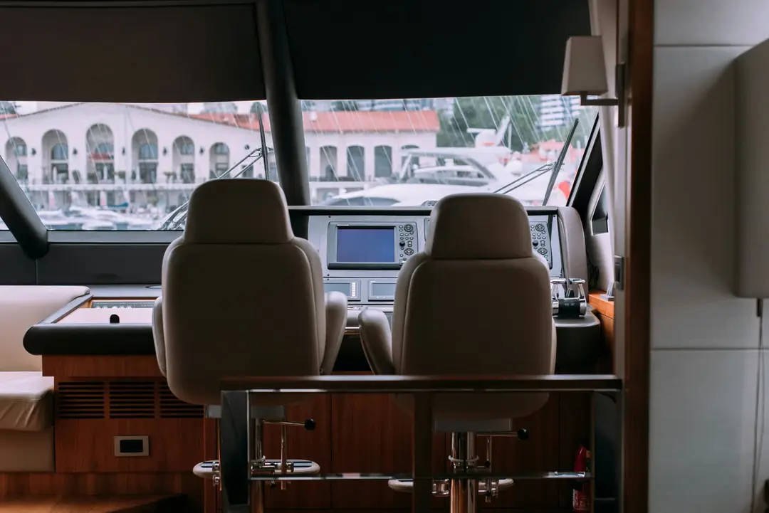 Interior helm station with two leather chairs, a chartplotter and a marina view through the windshield