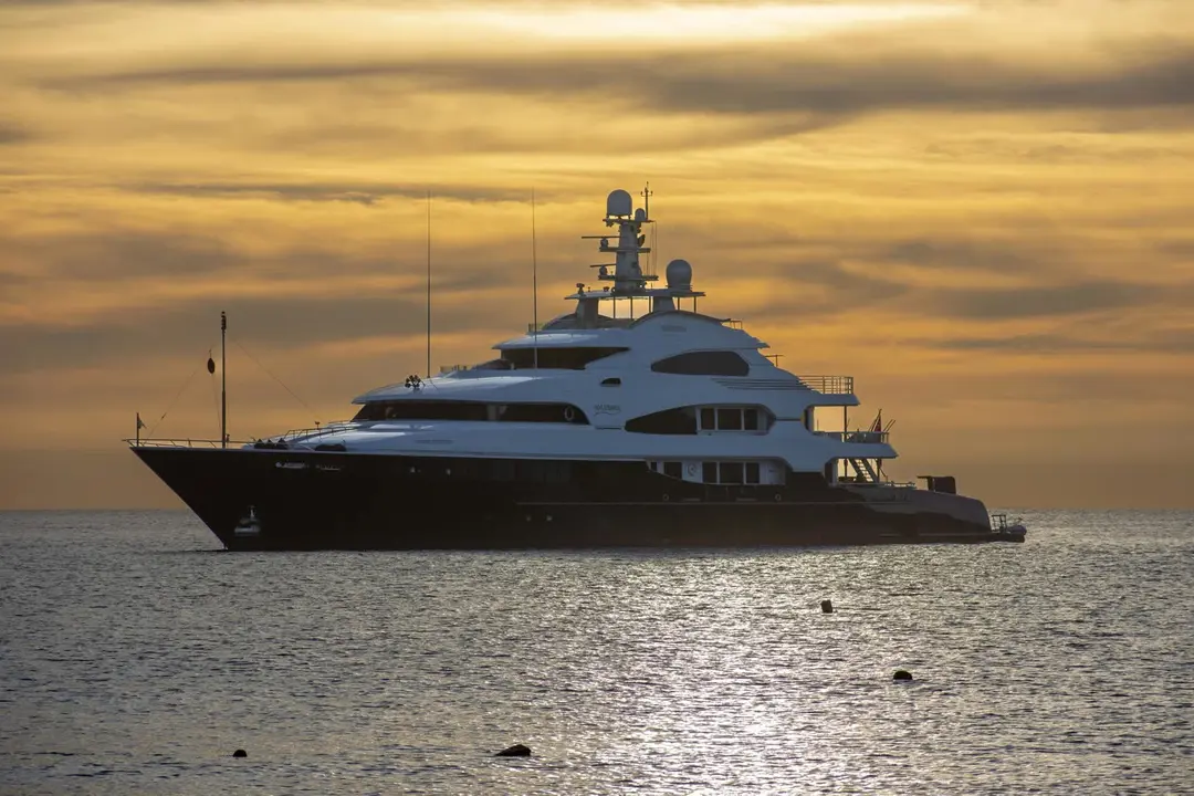 Large motor yacht lying at anchor, silhouetted against a golden sunset
