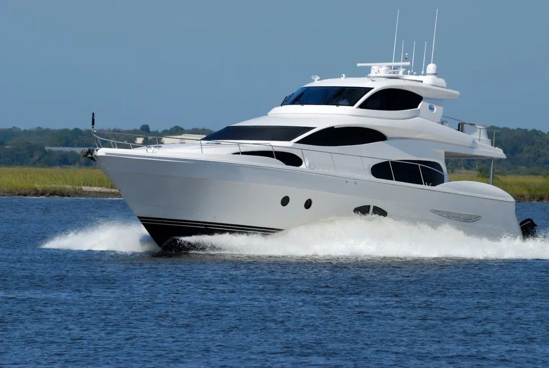 White motor yacht running at speed through a coastal channel, throwing a bow wave