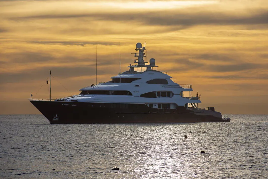 Superyacht at anchor on a calm sea beneath a golden sunset sky