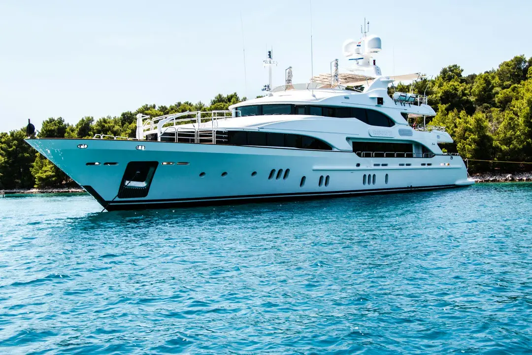 Pale-green superyacht lying at anchor in a pine-fringed turquoise bay